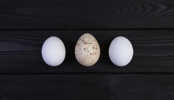 Goose egg and chicken eggs on a black wooden background. The difference in the size of eggs of various birds.