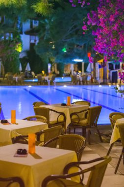 Gece Cafe, hizmet için akşam yemeği, mum, ışık, palm ağaçlar ve çiçeklerle, otelin diğer akşamlar bahçede havuz kenarında boş tablolar.