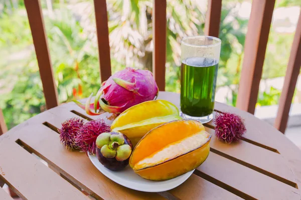 Mix of fresh fruits from Thailand, dragon fruit, rambutan, carambola, mangosteen and glass of emerald tea. Sliced beautiful fresh tropical fruits — Stock Photo, Image