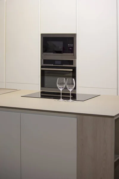 Design minimalista della cucina con isola. Cucina grigio-bianca e bicchieri di vino sul tavolo — Foto Stock