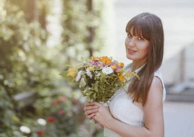 Parkta elinde bir buket ile bir yaz elbise güzel kız. Çiçeklerle yaz aylarında güzel bir kahverengi saçlı kadının portresi. Gelin