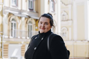 Şık bir siyah ceket gülümseyen kilolu esmer kadın. Turist öğrenci sırt çantasıyla dolaşıyor. Mutlu gülümseyen esmer artı boyutu kız Portresi