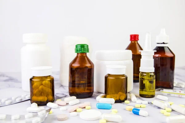 Πολλά διαφορετικά φιαλίδια και βάζα με χάπια και φάρμακα διαφορετικών χρωμάτων και μεγεθών σε λευκό μαρμάρινο φόντο. Ιατρικό υπόβαθρο — Φωτογραφία Αρχείου