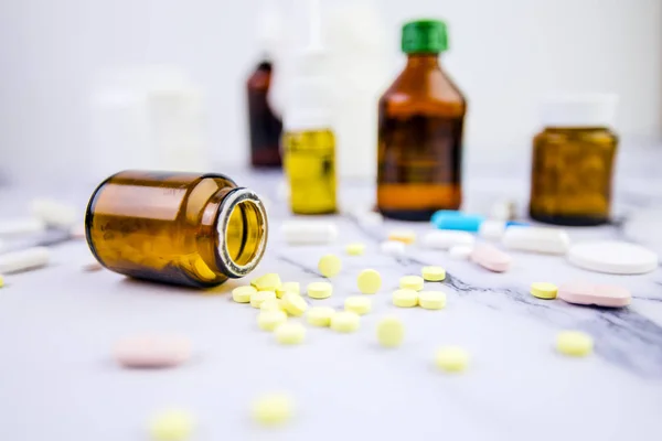 Βάζο με χάπια και φάρμακα διαφορετικών χρωμάτων και μεγεθών σε λευκό μαρμάρινο φόντο. Ιατρικό θέμα — Φωτογραφία Αρχείου