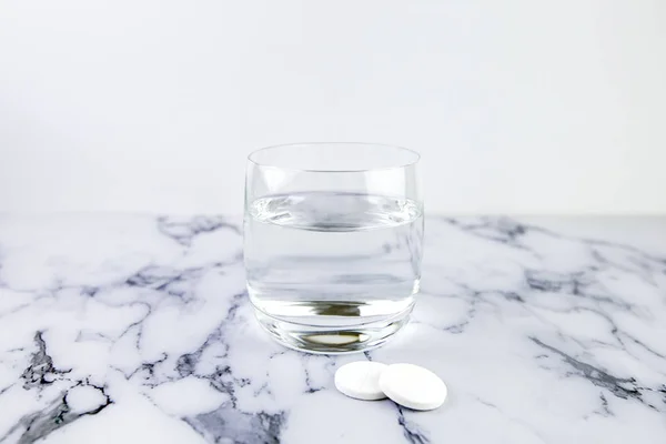 Αναβράζοντα δισκία και γυαλί με νερό. Φάρμακο ταχείας διάλυσης σε λευκό μαρμάρινο φόντο — Φωτογραφία Αρχείου