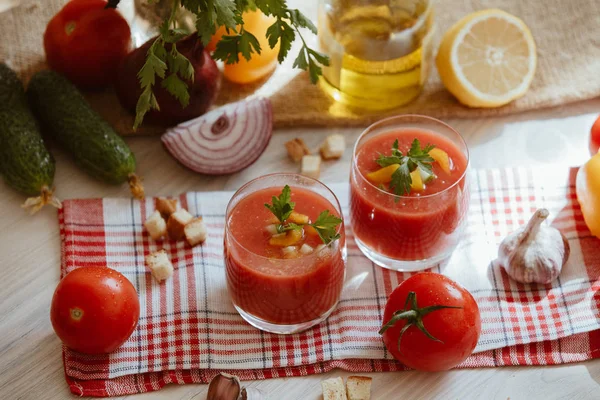 Sopa de tomate gazpacho en vaso con hierbas e ingredientes en la cocina. Una hermosa sopa de verano derramada en vasos rodeados de jugosas verduras — Foto de Stock