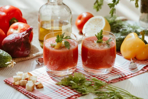 Sopa de tomate gazpacho en vaso con hierbas e ingredientes en la cocina. Una hermosa sopa de verano derramada en vasos rodeados de jugosas verduras . — Foto de Stock