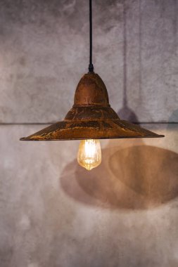 Çatı katındaki paslı metal avize, Edison ampulü, gri beton arka planda bulunan güzel kolye lambası.