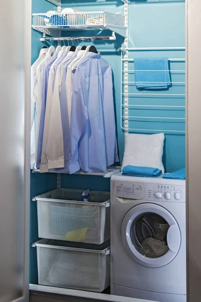 piles of clean clothes in laundry room. Laundry closet. Washing room, modern design with a laundry machine with hangers for clothes, an iron, shelves and a washing machine