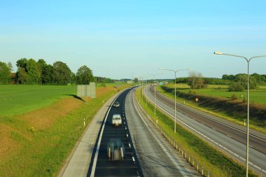 Birkaç arabalı Otoban yolu üzerinde renkli görünümü yukarıdaki. Yeşil yan alanlar ve mavi gökyüzü arka plan.