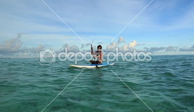 Sörf tahtası üzerinde oturan genç adam. Hint Okyanusu sakin suların. Beyaz bulutlar ile inanılmaz güzellik turkuaz su ve mavi gökyüzü. Maldivler.