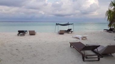 Hint Okyanusu'nda adasının muhteşem sahili. Yeşil bitkiler ve şezlonglar ile beyaz kum plaj. Şaşırtıcı turkuaz su ve beyaz bulutların üstünde mavi gökyüzü. Müthiş doğa manzara arka planları gerçek zamanlı.