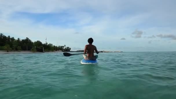 若い男がサーフボードの上に座って インド洋の穏やかな水 驚くべき美しさターコイズ ブルーの水と青空白い雲と モルディブ — ストック動画