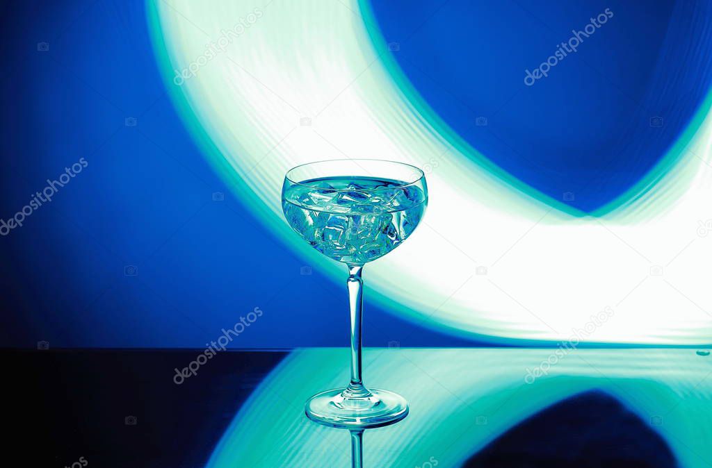 Beautiful view of alcohol drink with ice cubes in crystal glass on colorful background. 