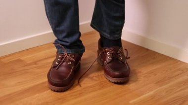  Adam koyarak ve koyu kahverengi ayakkabı bağlama kot pantolon. İnsanlar arka planlar.