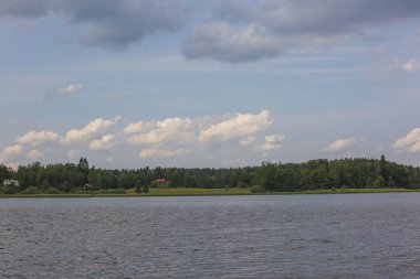 Yaz gününde göl de güzel bir manzara. Koyu göl su yüzeyi, yeşil uzun ağaçlar ve beyaz bulutlar ile mavi gökyüzü. İsveç, Avrupa.