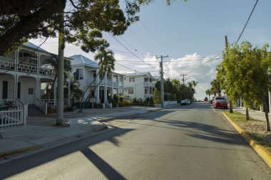 Key West caddelerinden birinin manzarası. Mavi arka planda eski evler ve büyük yeşil ağaçlar. Key West. Florida mı? Usa. 09.07.2019.