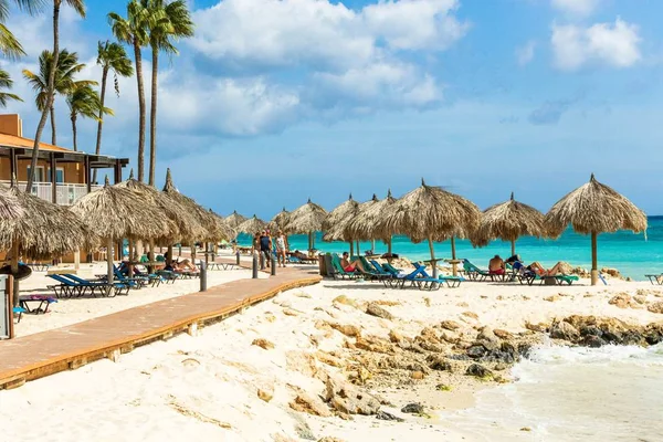 在酒店附近白色沙滩上的遮阳伞下 观光客在日光浴床上的景象 Tamarijn旅馆 Oranjestad 阿鲁巴 2019 — 图库照片