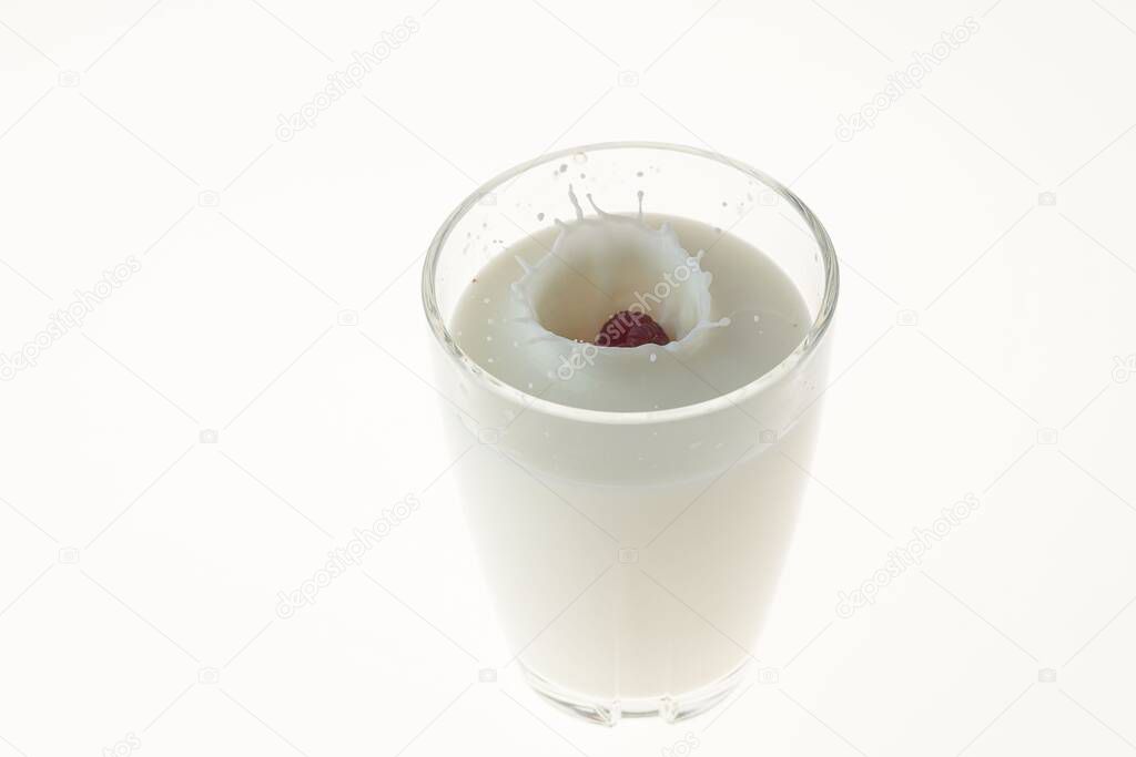 Close up view of red raspberry falling into milk on a white background.