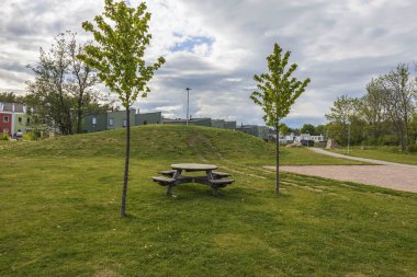 Yeşil çimenlerin üzerinde bankları ve mavi gökyüzünde beyaz bulutlu binaları olan güzel ahşap masa manzarası. İsveç. Avrupa.