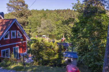 Güzel yukarıdan manzara manzarası. Geleneksel kırmızı ahşap ev, önünde misafir evi, arkasında orman olan göl. İsveç. Avrupa.