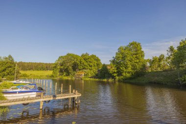 Ahşap iskele ve park etmiş motorlu tekne manzarası çok güzel. Mavi gökyüzü arka planında yeşil orman ağaçları. İsveç. Avrupa.
