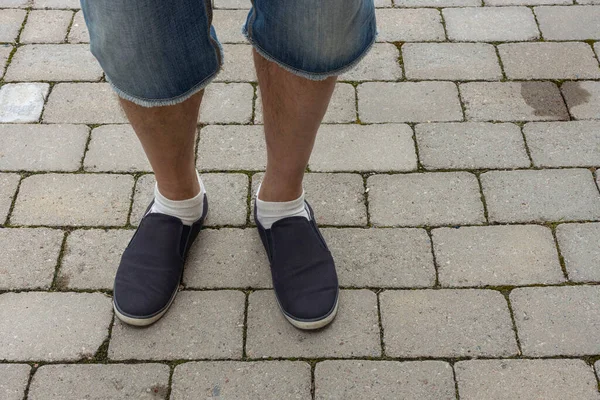 Close up view of male feet in black snickers on gray paving slabs. Summer men shoes.