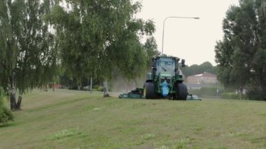 Modern çim biçme makinesindeki işçinin şehir çim tarlasıyla ilgilenmesi çok güzel bir manzara. 08.22.2020. Uppsala. İsveç. Avrupa.