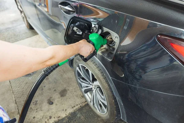 Woman pours fuel into the tank of a black car on gasoline station. Transportation concept. Beautiful backgrounds.