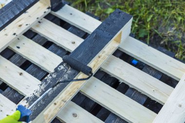 Boya silindiri tutan el görüntüsü ve özel siyah ağaç yağı ile ahşap palet tedavi.