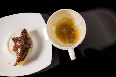 Boş fincanın görüntüsünü kapatın. Kahvenin geri kalanı ve siyah arka planda izole edilmiş çikolatalı çörek. Yiyecek ve içecek konsepti.