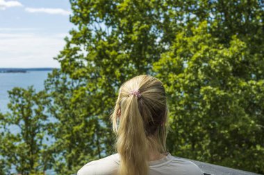 Güzel bir yaz Baltık deniz manzarası. Genç sarışın kadın yeşil ağaçların arasından denize bakıyor.. 