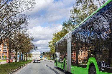 Arka planda ağaçlar ve konut binaları olan yeşil şehir otobüsü şehir caddesinde gidiyor.. 