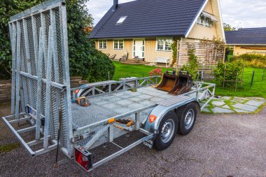 Bahçeli ve yeşil çimenli konut evinin önüne park etmiş kazıcı kovalarıyla dolu metal bir karavan.. 