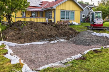 Takeuchi TB225 mini kazıcı inşaat sırasında güneş panelli sarı ahşap evin yanında duruyor..