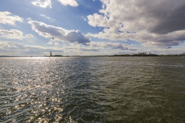 Arka planda Özgürlük Anıtı olan New York Limanı ve bulutlu gökyüzü olan Ellis Adası. - New York. ABD.