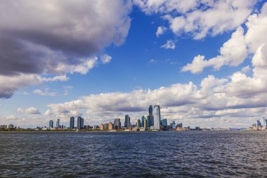 Hudson Nehri, arka planda modern Jersey şehrinin silueti ve dramatik bulutlu mavi gökyüzü. - New York. ABD.