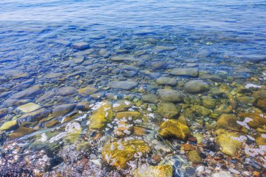 Açık mavi Ege Denizi 'nin arka planında şeffaf suda küçük yüzey dalgaları olan renkli taşlar. Yunanistan.