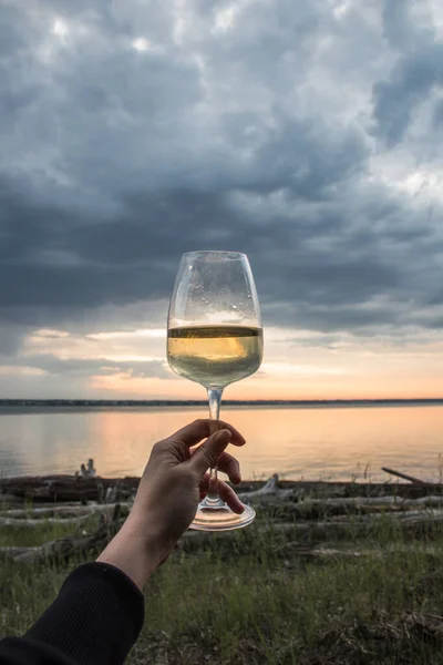 Női kéz egy pohár borral. Kényelmes móló naplemente a tengeren. Víz és kilátás az égre, gyönyörű táj. Kaland Stock Fotó