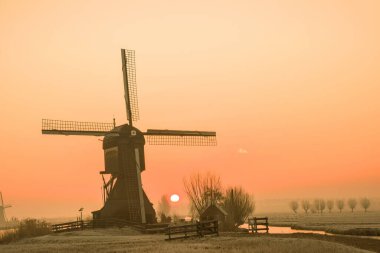 Hollanda 'da sabahın erken saatlerinde rüzgâr değirmeni siluetleriyle tipik bir kırsal bölge.