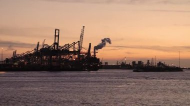 Günbatımında uluslararası nakliye limanındaki kargo gemisi konteynırlarını parlak dalga yansımalı stratocumulus bulutları ve Rotterdam, Hollanda 'da kırmızı canlı gökyüzü ile dolduruyor.