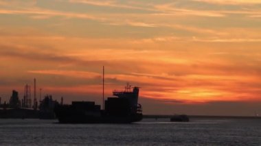 Kargo gemisi gün batımında uluslararası nakliye limanına sensör tozu, toprak ve nem gibi görünen stratocumulus bulutları ve Rotterdam, Hollanda 'daki parlak su yansıması ile giriyor.