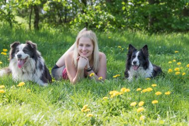 Genç Sarışın kadın gülüyor iki sınır Collies köpekler arasında açık havada yalan söylüyor. Kadın ve köpek kameraya arıyoruz.