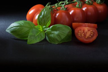 Bir yaprak siyah taş masanın üzerinde yatan ön planda dilimlenmiş domates ve fesleğen ile düşük anahtar atış çalılar domates. Atış daha düşük bir açıda ve fotoğrafın altındaki metni boş alanı olan.