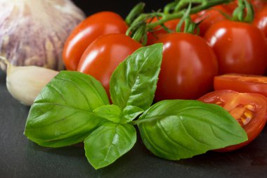 Çalılar domates closeup görünümüyle bir yaprak fesleğen, sarımsak, sarımsak ve dilimlenmiş domates siyah taş masanın üzerinde yatan karanfil. 