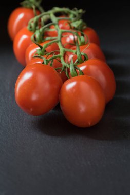 Siyah taş masanın üzerinde yatan çalılar domates düşük anahtar atış. Koyu arka plan üzerine kadar. Dikey olarak.