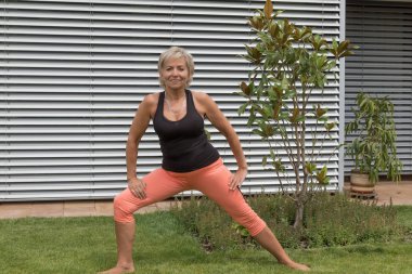 Gülümseyen kıdemli sarışın kadın bahçede açık kamera bakarak onun uzanıyor yapıyor