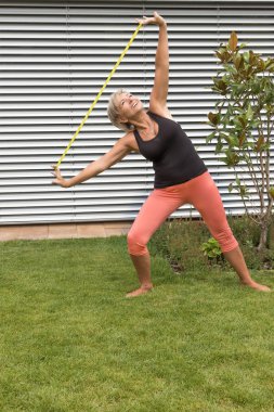 Gülümseyen kıdemli sarışın kadının elinde gerilmiş kauçuk bakarak onun uzanıyor yapması. 