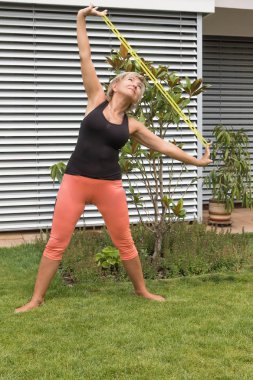 Üst düzey sarışın kadının onun uzanıyor bahçede açık bir lastik ile yapması germe. Dikey olarak. 