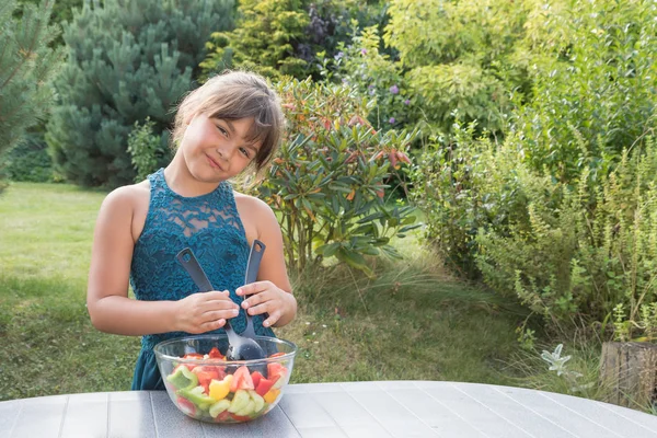 Attractive  little girl is a stirring fresh vegetable salad in the garden.